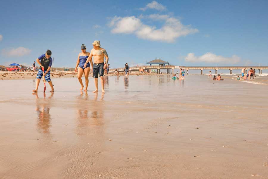 Families stroll through the low tide at a Texas gulf beach