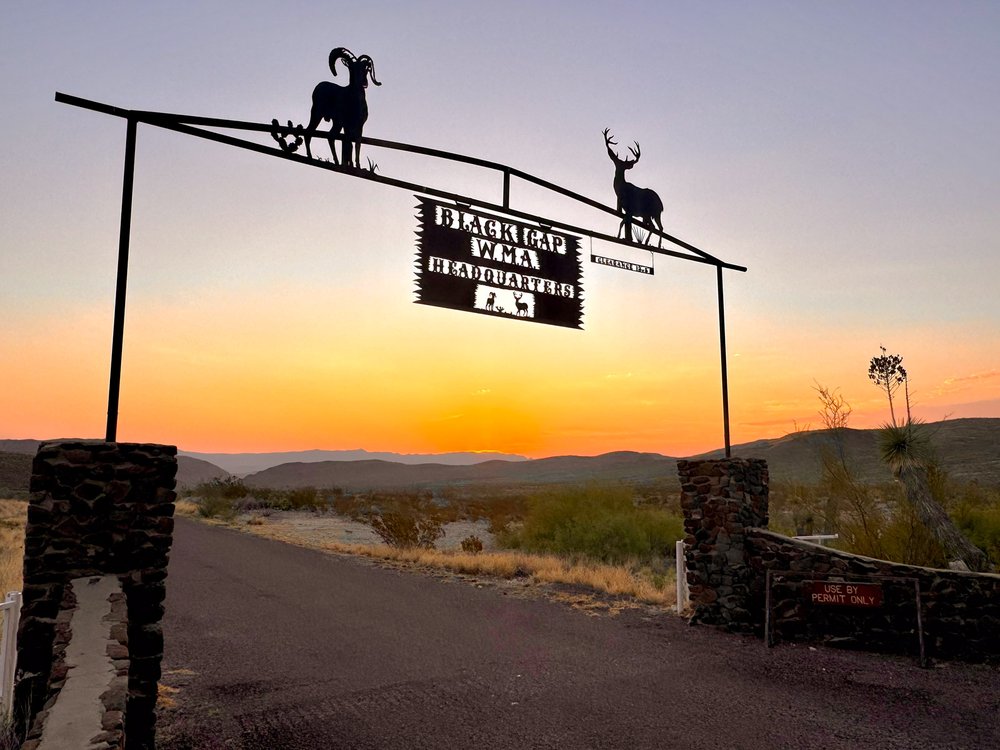 A sign hangs over a gate with a sunset in the background