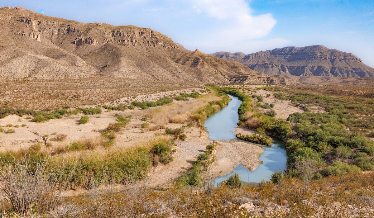 The rio grande river winds through the landscape with mountains in the background