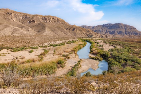 The rio grande river winds through the landscape with mountains in the background