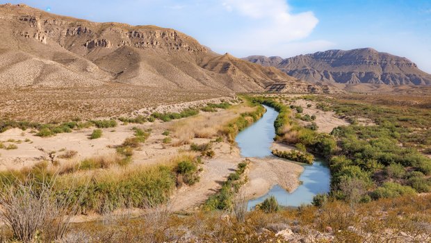 The rio grande river winds through the landscape with mountains in the background