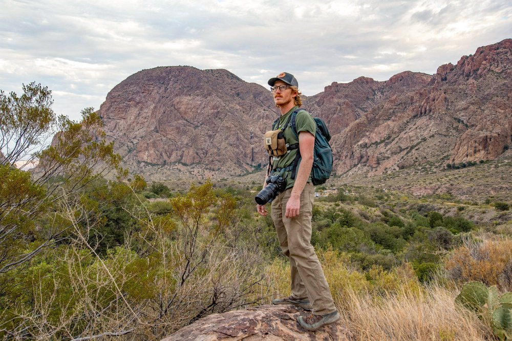 A man looks off into the distance wearing binoculars and a camera.