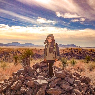 A little boy wearing sunglasses poses on top of a pile of rocks.