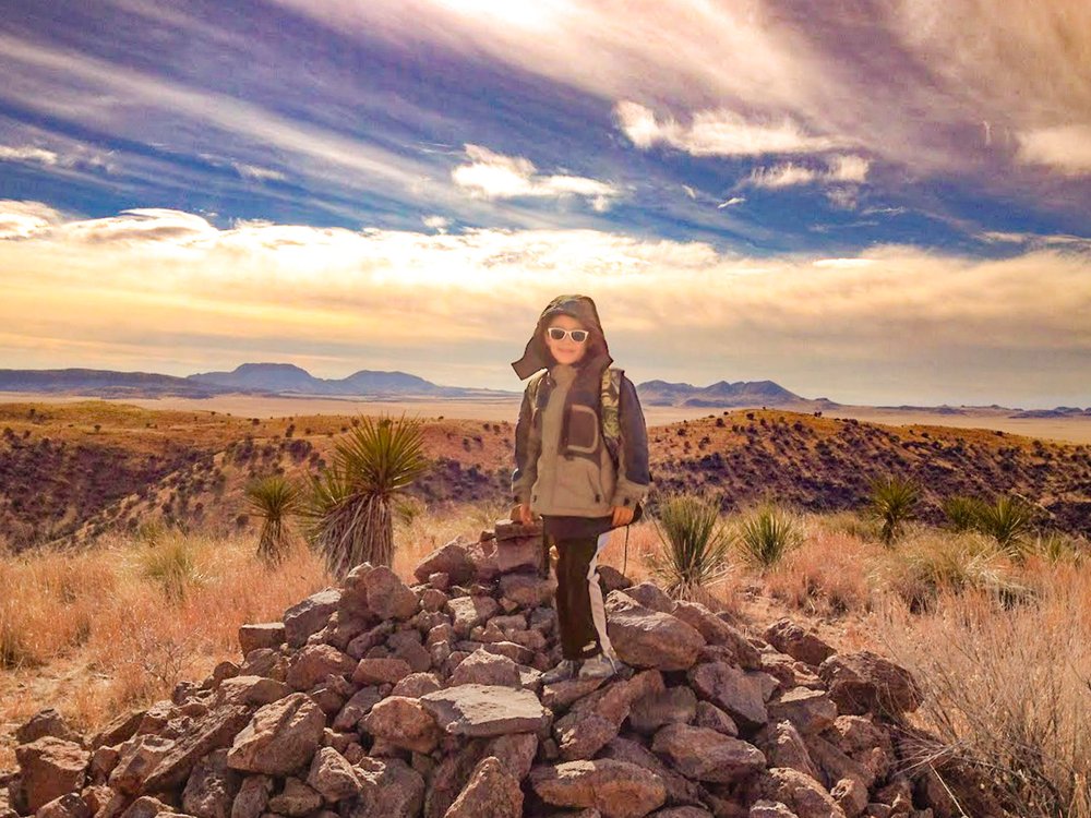 A little boy wearing sunglasses poses on top of a pile of rocks.