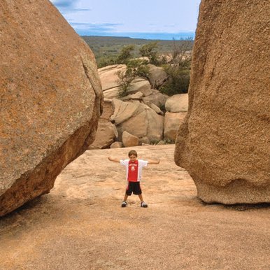 A little boy stretches out his arms between two large bolders