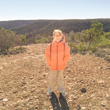 Little boy in an orange jacket stands on a hilltop overlook