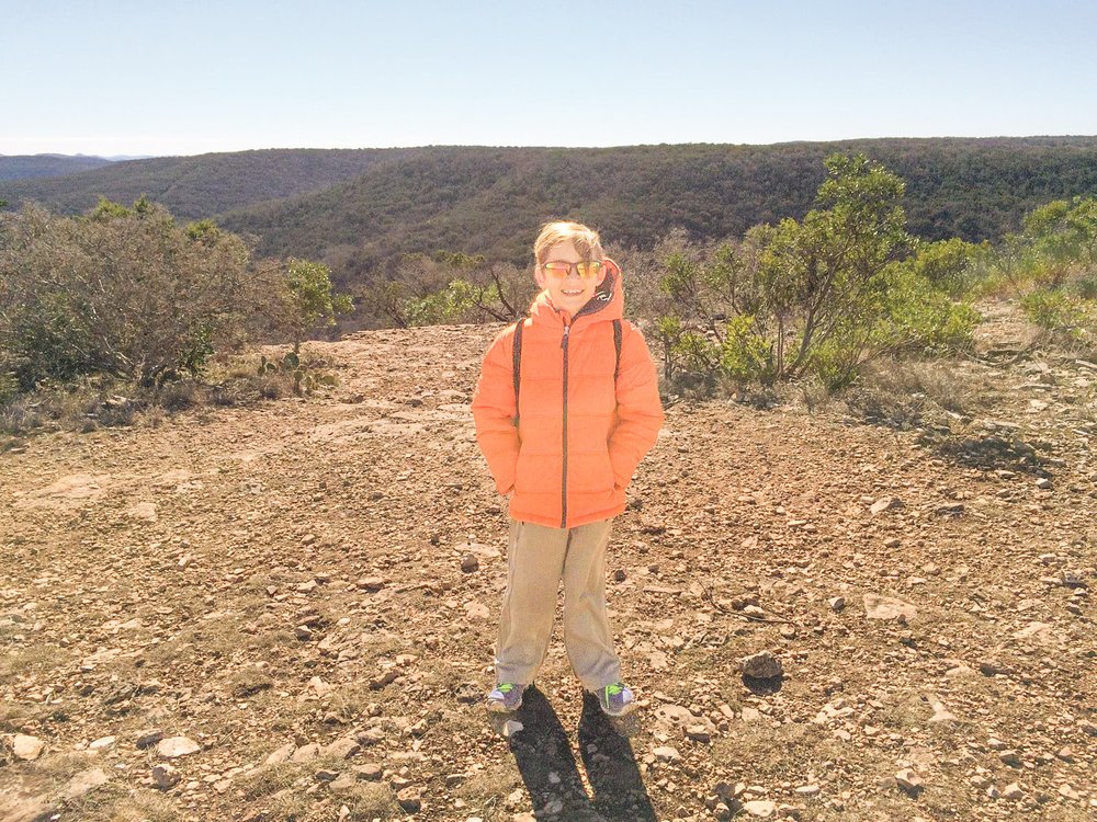 Little boy in an orange jacket stands on a hilltop overlook