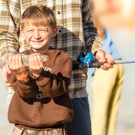 A little boy with a big grin on his face holds up his fish catch.