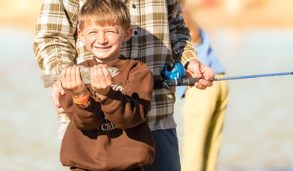 A little boy with a big grin on his face holds up his fish catch.