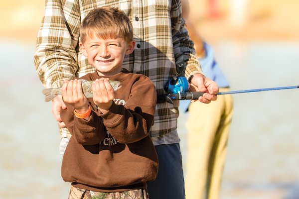 A little boy with a big grin on his face holds up his fish catch.