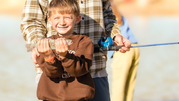 A little boy with a big grin on his face holds up his fish catch.