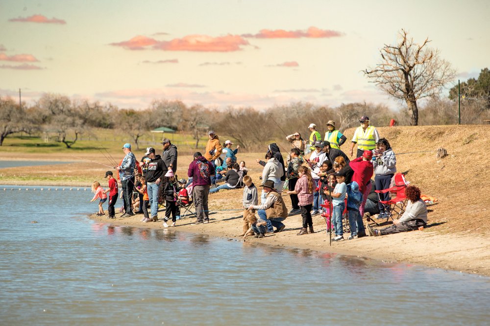 A large group of parents and children fish along the shore.