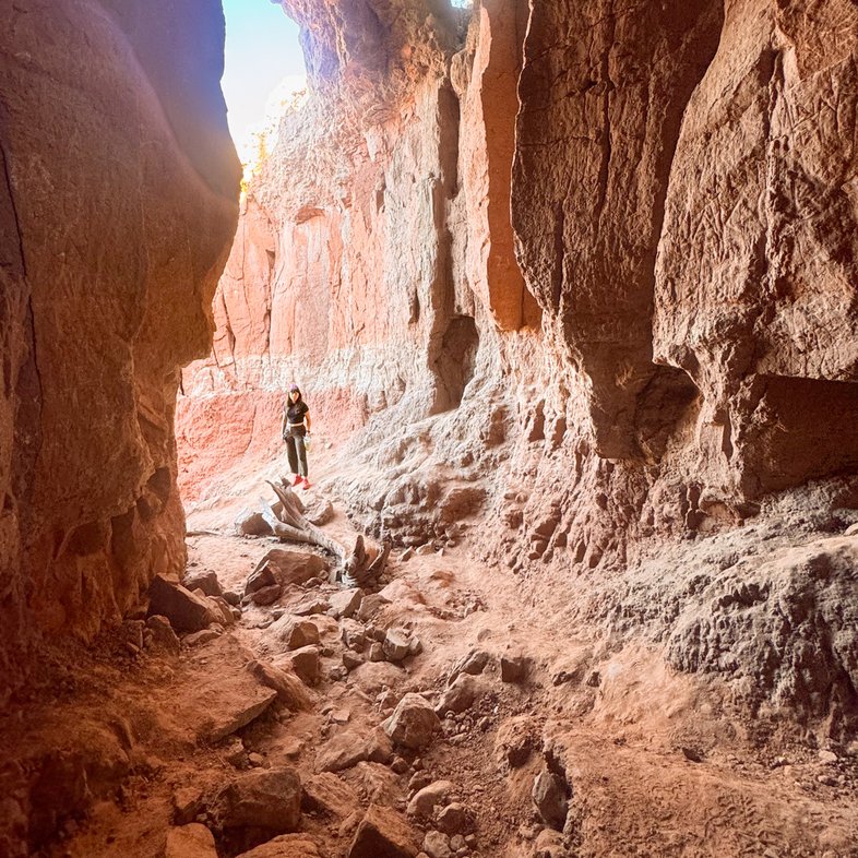 A woman looks into the mouth of a cave with a canyon horizon in the background