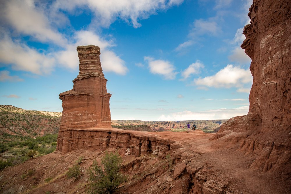 Two men sit next to a hoodoo shaped like a lighthouse.