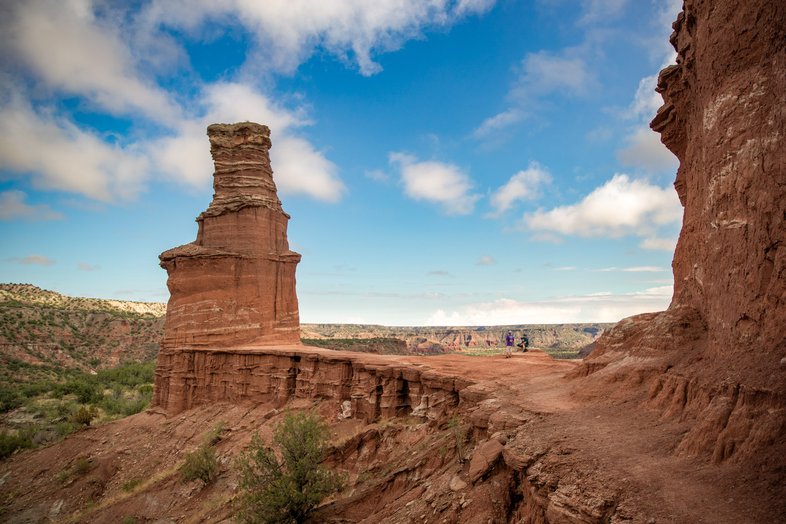 Two men sit next to a hoodoo shaped like a lighthouse.