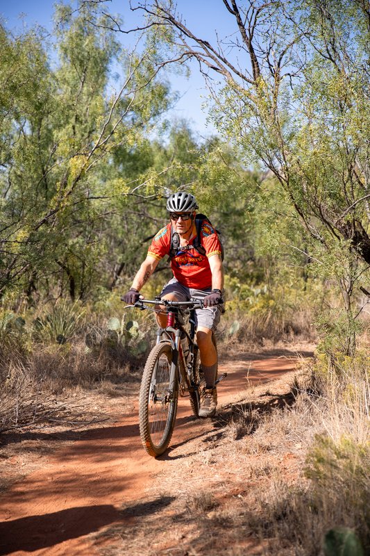 A man wearing a red shirt bikes along a trail