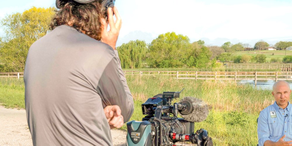 Abe Moore stands behind his camera conducting an interview for the TPWD PBS Tv Show