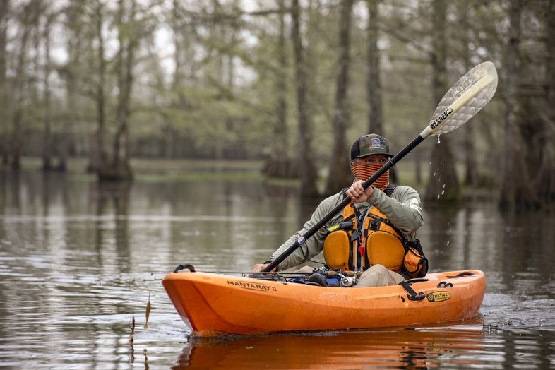 Person paddling in a kayak with cypress trees in the background.