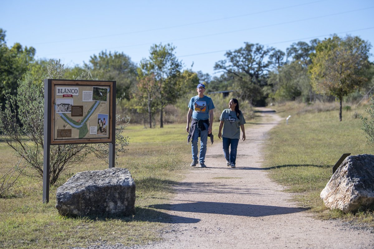 People walking on the Pumphouse trail by an interpretive sign in Blanco State Park