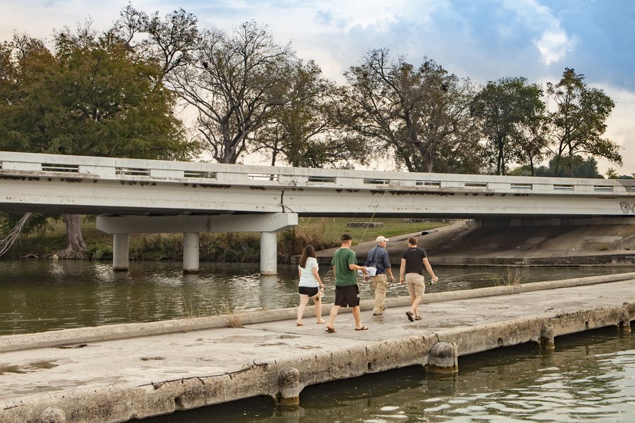 People walking across the Blanco River next to a bridge.