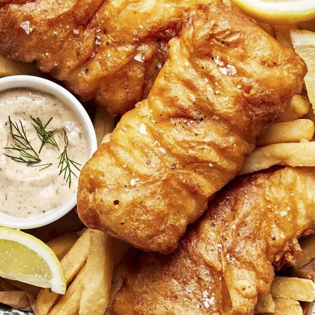 Fried fish on a plate with french fries, sauce and lemon wedges