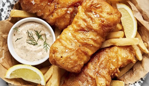 Fried fish on a plate with french fries, sauce and lemon wedges