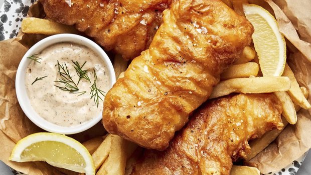 Fried fish on a plate with french fries, sauce and lemon wedges