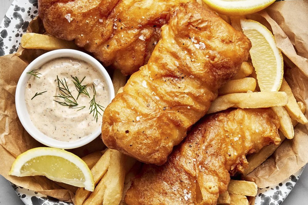 Fried fish on a plate with french fries, sauce and lemon wedges