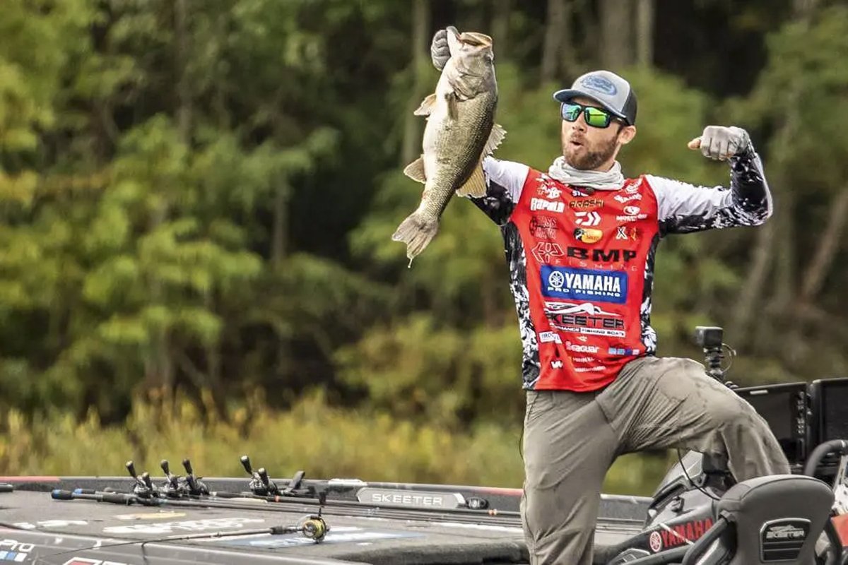 A man standing on a boat holds up a big bass