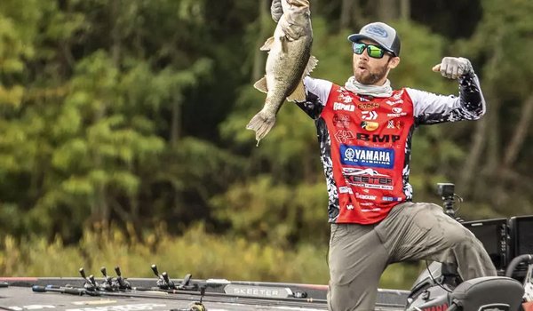 A man standing on a boat holds up a big bass