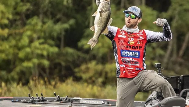 A man standing on a boat holds up a big bass
