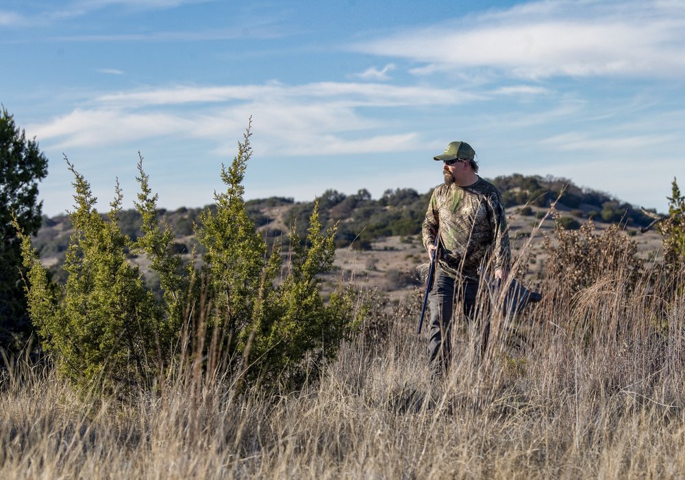 Hunter walking through a field with a gun.