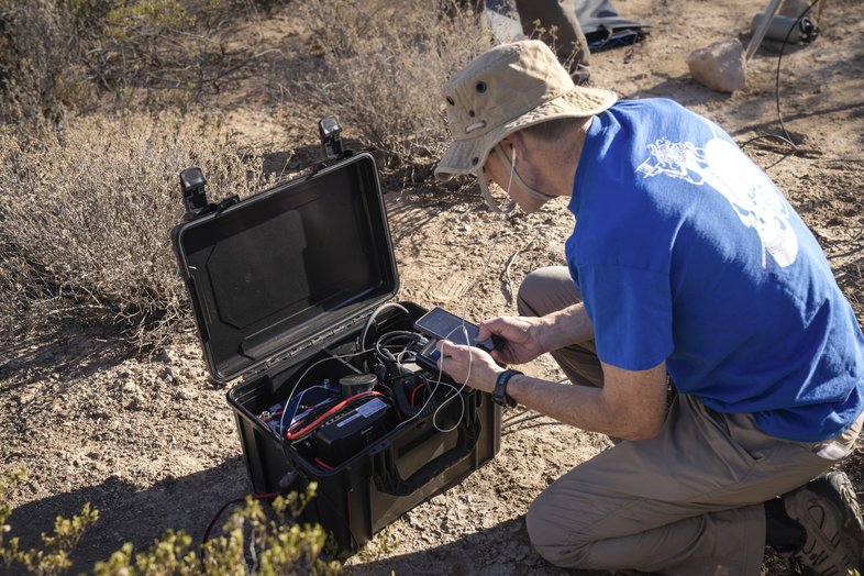 Person in a hat kneeling while looking in a box of wires.