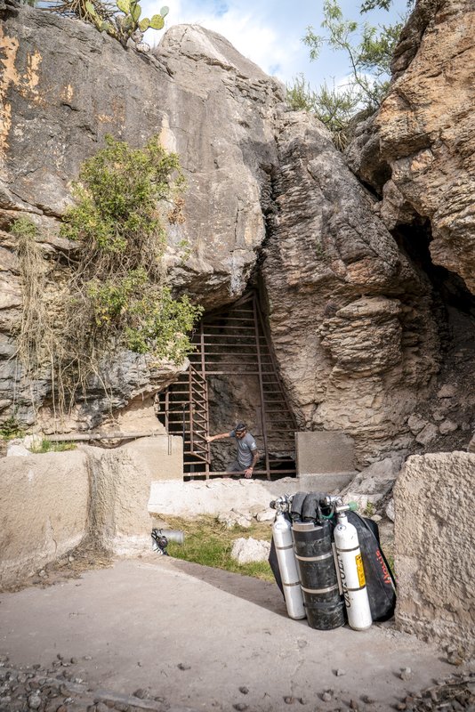 Oxygen tanks and a person opening a gate into a cave.