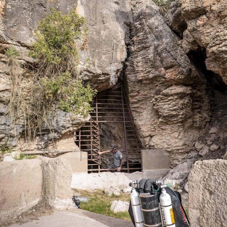 Oxygen tanks and a person opening a gate into a cave.