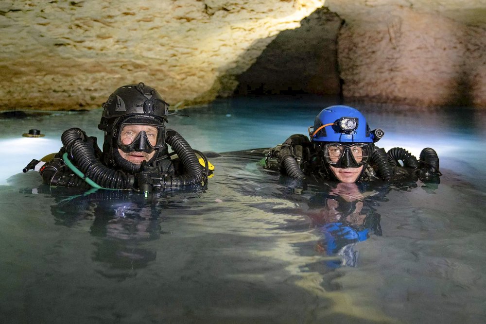 Two scuba divers at the surface of the water in a cave.