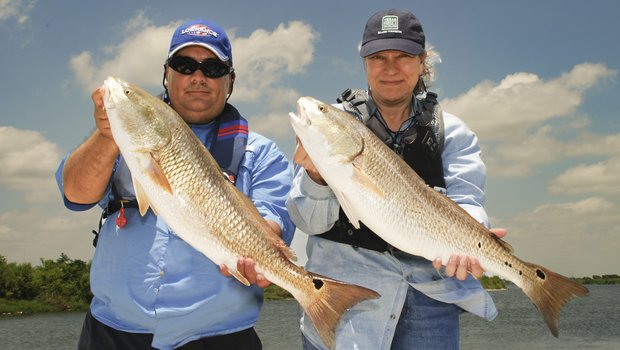 Two people holding up large fish that they caught.