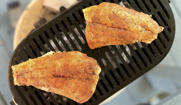 Red fish cooking on a grill.