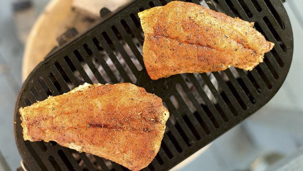 Red fish cooking on a grill.