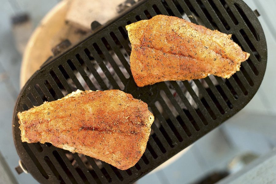 Red fish cooking on a grill.