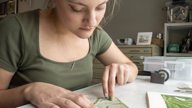 Artist Raylee Schobel pressing inked printing blocks to paper.