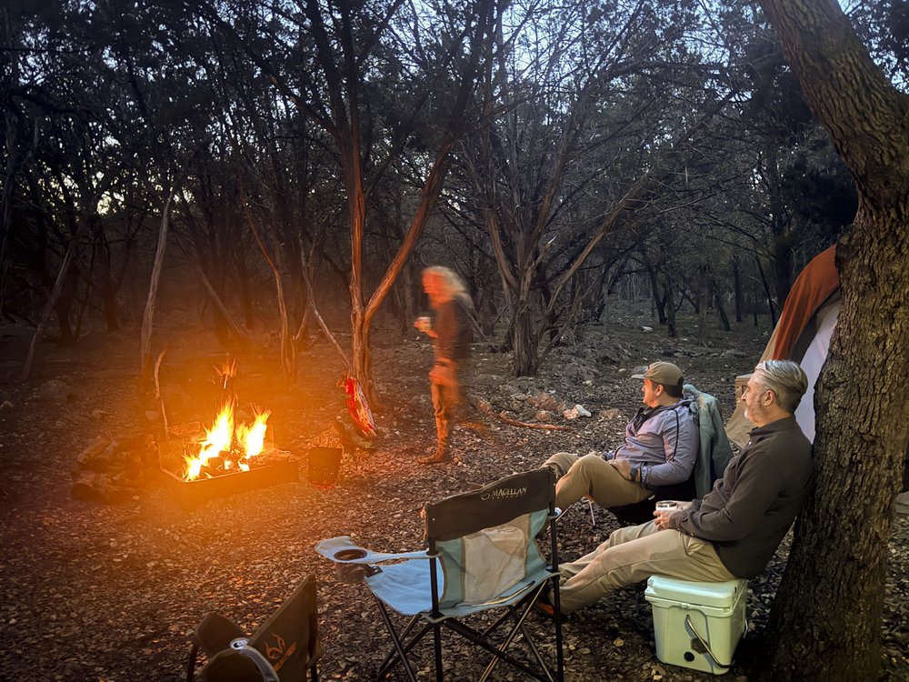 Three people around a campfire at dusk