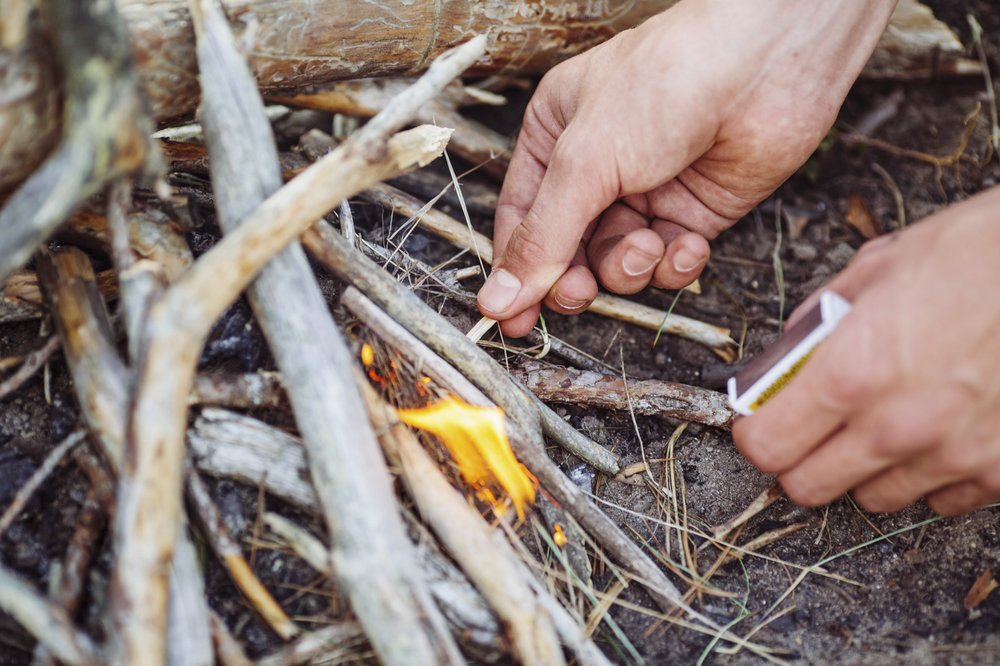 A person's hands lighting a campfire with a match