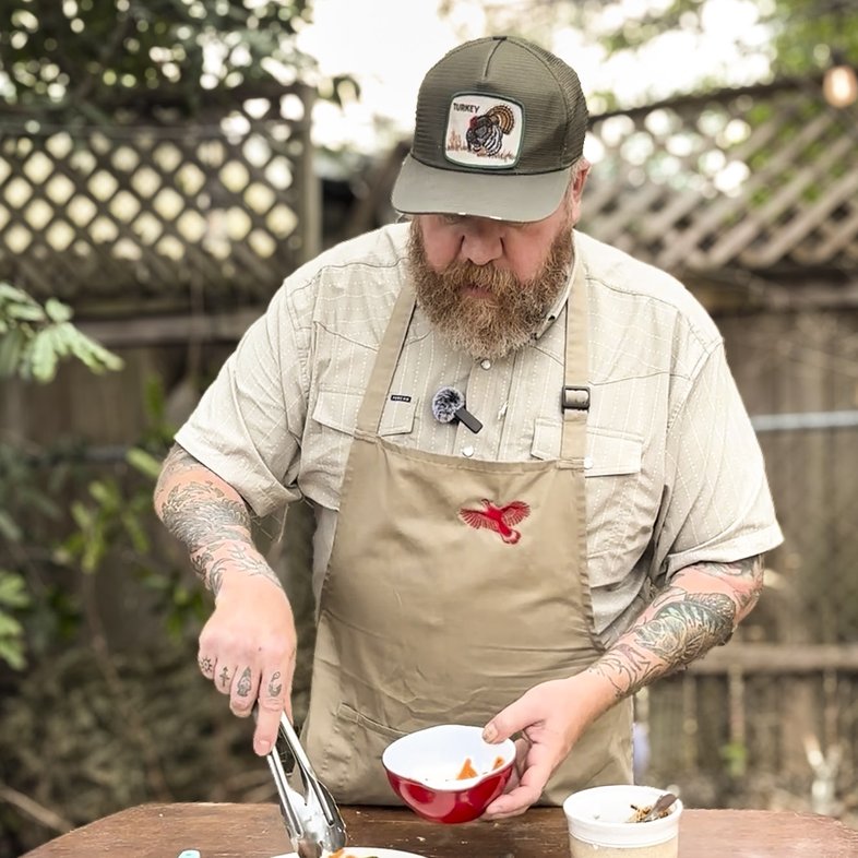 A man uses tongs to place cucumber salad on a plate next to breaded turkey.