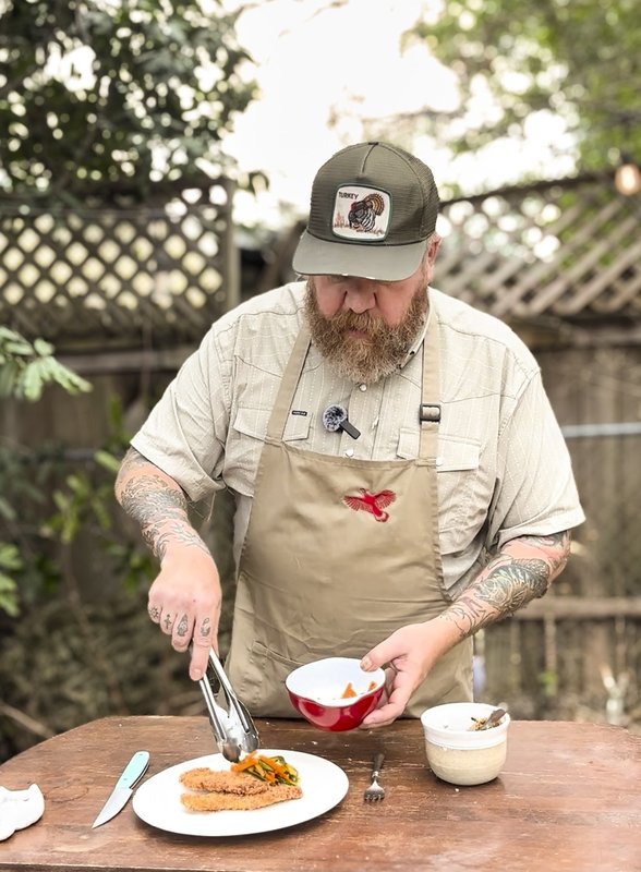 A man uses tongs to place cucumber salad on a plate next to breaded turkey.