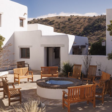 A white adobe lodge, featuring a courtyard with wooden chair seating around a firepit
