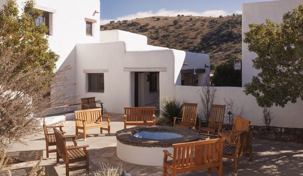 A white adobe lodge, featuring a courtyard with wooden chair seating around a firepit