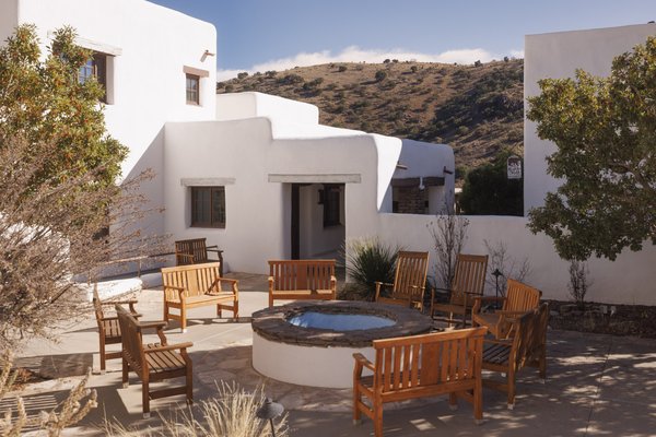 A white adobe lodge, featuring a courtyard with wooden chair seating around a firepit