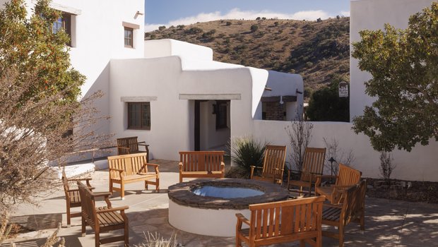 A white adobe lodge, featuring a courtyard with wooden chair seating around a firepit
