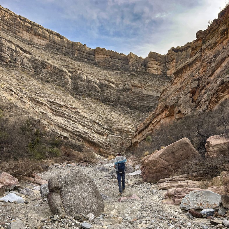 A person with a back pack walking a trail in a canyon at Big Bend Ranch State Park.